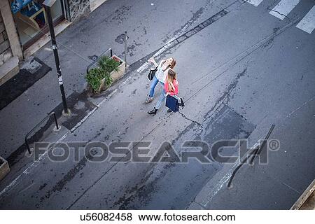 Stock Photo - High angle view of two female friends laughing whilst strolling on city street. Fotosearch