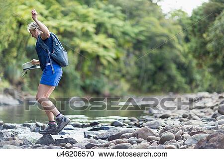 Stock Image - "Hiker walking among stones in shallow stream, Waima Forest, North Island, NZ". Fotosearch