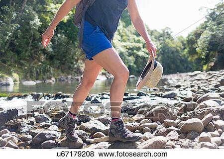 Stock Photo - "Hiker walking among stones in shallow stream, Waima Forest, North Island, NZ". Fotosearch