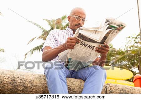 Stock Photography - "Low angle view of mature man reading newspaper, Ipanema beach, Rio De Janeiro, Brazil". Fotosearch