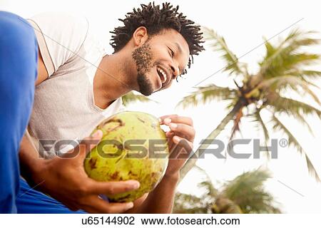 Stock Image - "Low angle view of mid adult man drinking coconut milk, Ipanema beach, Rio De Janeiro, Brazil". Fotosearch