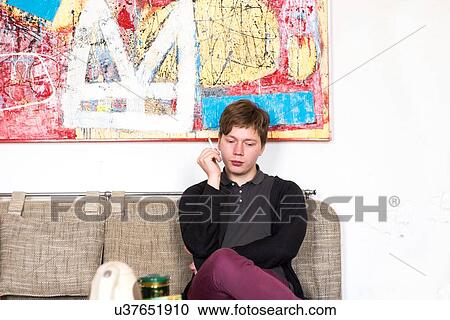 Stock Image - Male artist smoking cigarette whist sitting on studio sofa. Fotosearch