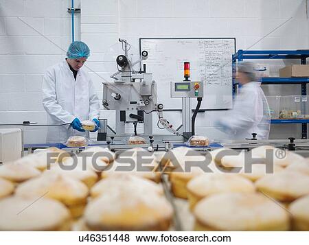 Stock Photo - Male baker putting cakes on packaging line in cake factory. Fotosearch