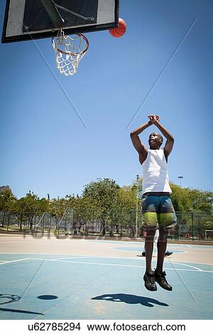 Picture - Male basketball player throwing ball toward basketball hoop. Fotosearch