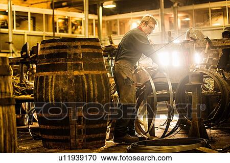 Stock Image - Male cooper making whisky casks in cooperage. Fotosearch