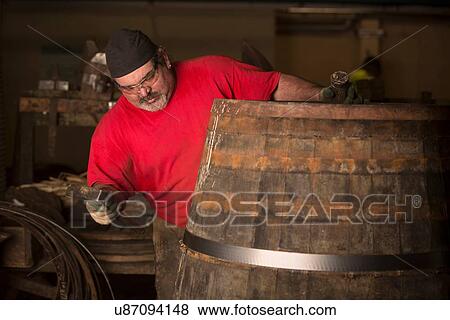 Stock Photo - Male cooper using hammer in cooperage with whisky casks. Fotosearch