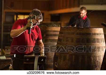 Stock Photograph - Male cooper using hammer in cooperage with whisky casks. Fotosearch