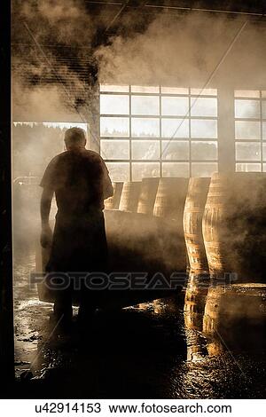Stock Image - Male cooper working in cooperage with whisky casks. Fotosearch