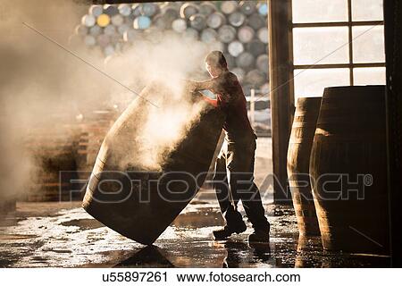 Stock Image - Male cooper working in cooperage with whisky casks. Fotosearch