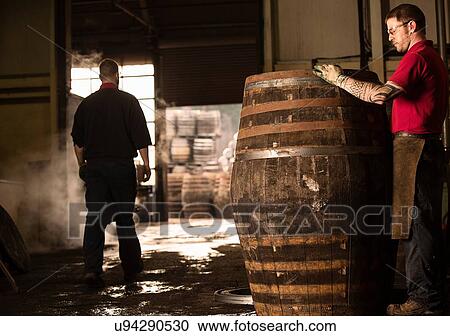Stock Image - Male cooper working in cooperage with whisky cask. Fotosearch