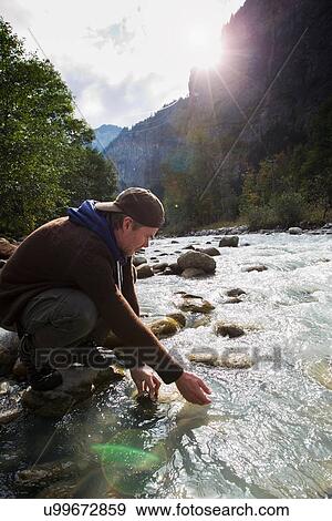 Stock Photo - "Male hiker crouching down by river, Lauterbrunnen, Grindelwald, Switzerland". Fotosearch