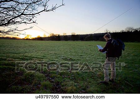 Stock Image - Male hiker reading map in field at sunset. Fotosearch