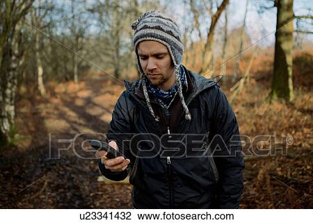 Stock Image - Male hiker reading texts on smartphone in woods. Fotosearch