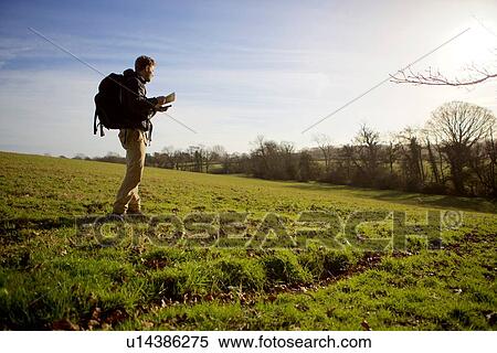 Male hiker walking in field whilst reading folding map View Large Photo Image Stock Photography - Male hiker walking in field whilst reading folding map. Fotosearch