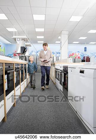 Stock Photograph - Male shopper and son checking prices on digital tablet in electronics store. Fotosearch