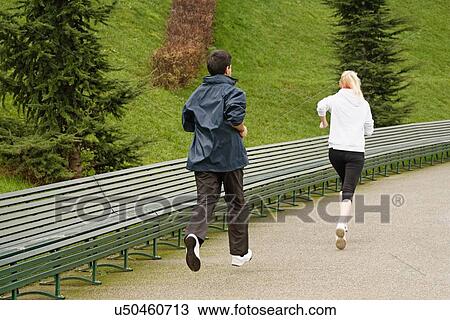 Stock Image - "Man and woman running along pathway, rear view". Fotosearch