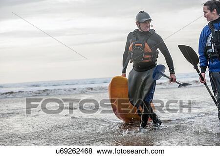 Stock Photo - Man and woman walking with sea kayak. Fotosearch