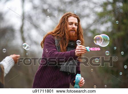 Stock Image - Man blowing soap bubbles in countryside. Fotosearch