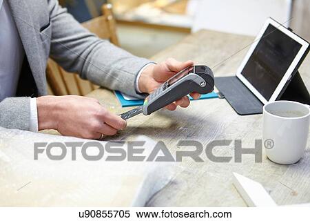 Stock Photography - Man buying online with credit card in picture framers workshop. Fotosearch