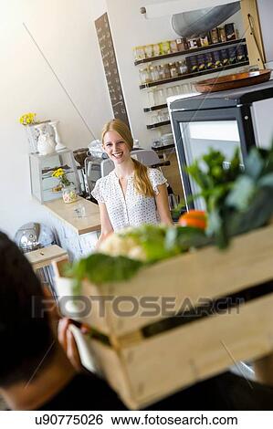 Stock Photograph - Man delivering crate of vegetables to shopkeeper. Fotosearch
