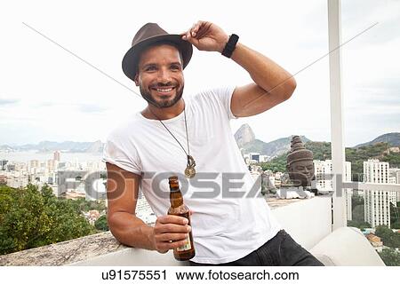 Stock Image - "Man drinking on terrace, Sugarloaf Mountain in background, Rio, Brazil". Fotosearch