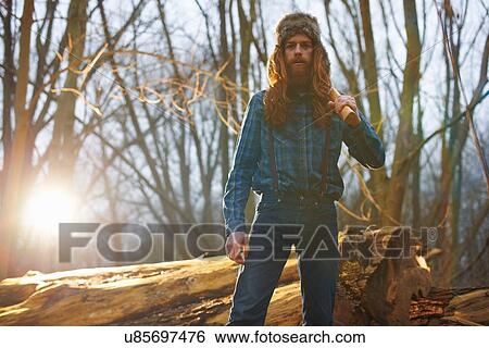 Stock Photograph - Man in trapper hat chopping wood in countryside. Fotosearch