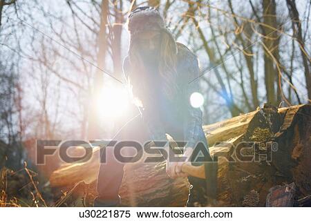 Stock Photography - Man in trapper hat chopping wood in countryside. Fotosearch