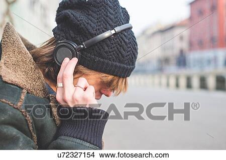 Picture - "Man listening to music through headphones on kerb, Milan, Italy". Fotosearch