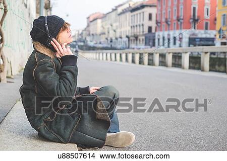 "Man listening to music through headphones on kerb, Milan, Italy" View Large Photo Image Picture - "Man listening to music through headphones on kerb, Milan, Italy". Fotosearch