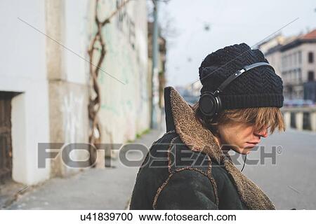 "Man listening to music through headphones on kerb, Milan, Italy" View Large Photo Image Stock Image - "Man listening to music through headphones on kerb, Milan, Italy". Fotosearch