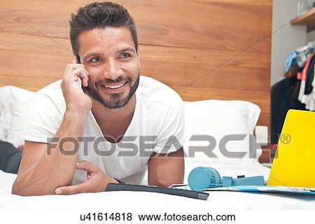 Stock Photo - Man lying on bed using phone. Fotosearch