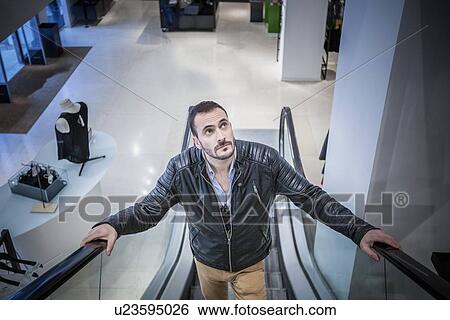 Stock Photograph - Man moving up escalator in shopping mall. Fotosearch