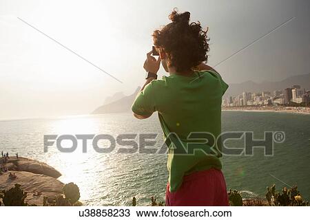Stock Image - "Man taking photo of view, Ipanema Beach, Rio de Janeiro, Brazil". Fotosearch
