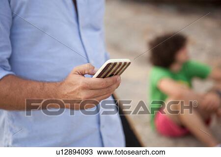 "Man using smartphone, son sitting in background" View Large Photo Image Stock Image - "Man using smartphone, son sitting in background". Fotosearch