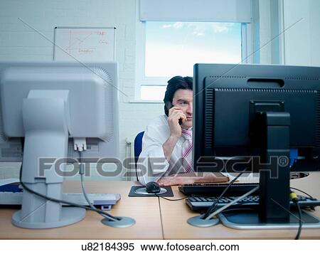 Man using telephone and working on computer at desk View Large Photo Image Stock Photography - Man using telephone and working on computer at desk. Fotosearch