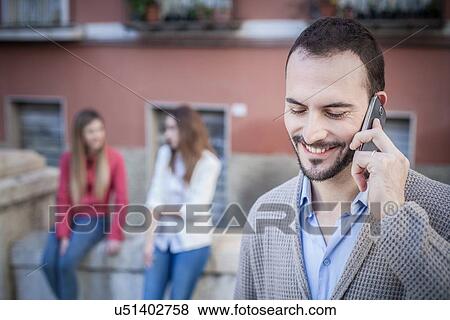 "Man with female friends talking on smartphone, Cagliari, Sardinia, Italy" View Large Photo Image Stock Photo - "Man with female friends talking on smartphone, Cagliari, Sardinia, Italy". Fotosearch
