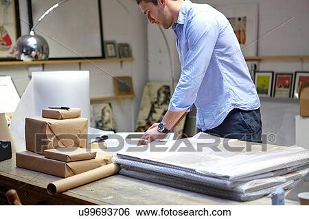 Man wrapping frames in bubble wrap on table in picture framers workshop View Large Photo Image Stock Photograph - Man wrapping frames in bubble wrap on table in picture framers workshop. Fotosearch
