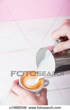 Stock Photograph - Mans hands pouring frothed milk into coffee cup. Fotosearch
