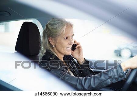 Stock Image - Mature businesswoman chatting on smartphone whilst driving car. Fotosearch