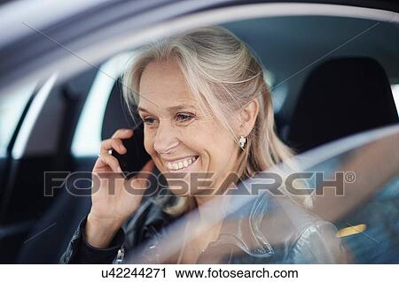 Stock Image - Mature businesswoman chatting on smartphone in car. Fotosearch