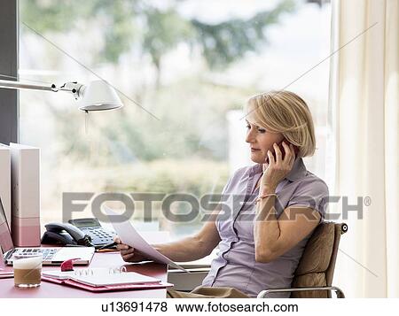Mature businesswoman talking on smartphone at home desk View Large Photo Image Stock Photo - Mature businesswoman talking on smartphone at home desk. Fotosearch