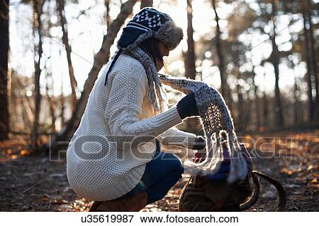 Stock Photo - Mature female backpacker putting on scarf in forest. Fotosearch