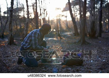 Picture - Mature male backpacker stacking logs for campfire in forest. Fotosearch