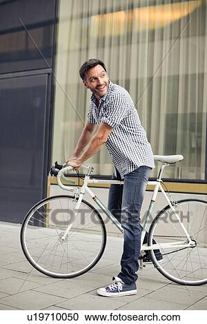 Mature male cyclist looking back on city street View Large Photo Image Stock Image - Mature male cyclist looking back on city street. Fotosearch