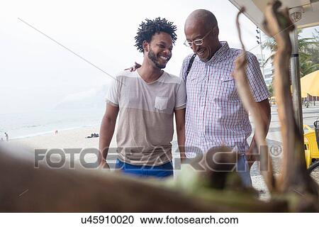 Stock Image - "Mature man and son chatting at bar on Ipanema beach, Rio De Janeiro, Brazil". Fotosearch
