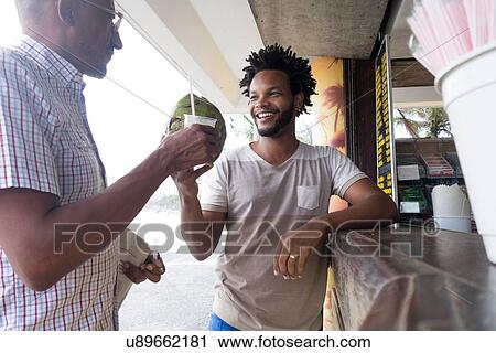 Stock Image - "Mature man and son toasting drinks at bar on Ipanema beach, Rio De Janeiro, Brazil". Fotosearch