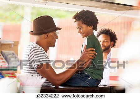 Stock Image - "Mature man chatting to grandson sitting on bar, Ipanema beach, Rio De Janeiro, Brazil". Fotosearch