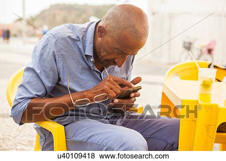 Stock Photo - "Mature man concentrating on smartphone at bar on Ipanema beach, Rio De Janeiro, Brazil". Fotosearch