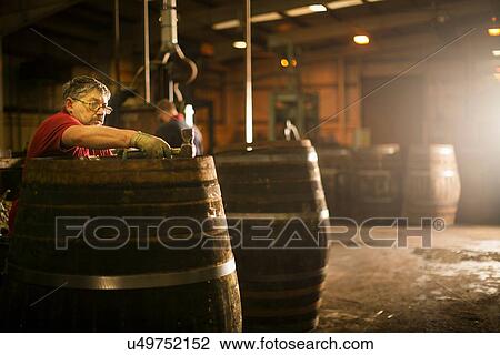 Stock Image - Mature man making whisky cask in cooperage. Fotosearch