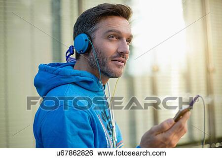 Mature man on city street choosing headphone music on smartphone View Large Photo Image Stock Photograph - Mature man on city street choosing headphone music on smartphone. Fotosearch